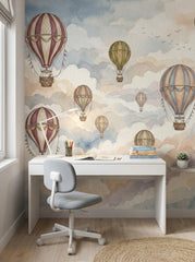 Hot air balloon wallpaper with burgundy, green and blue vintage balloons behind a white kids study desk.