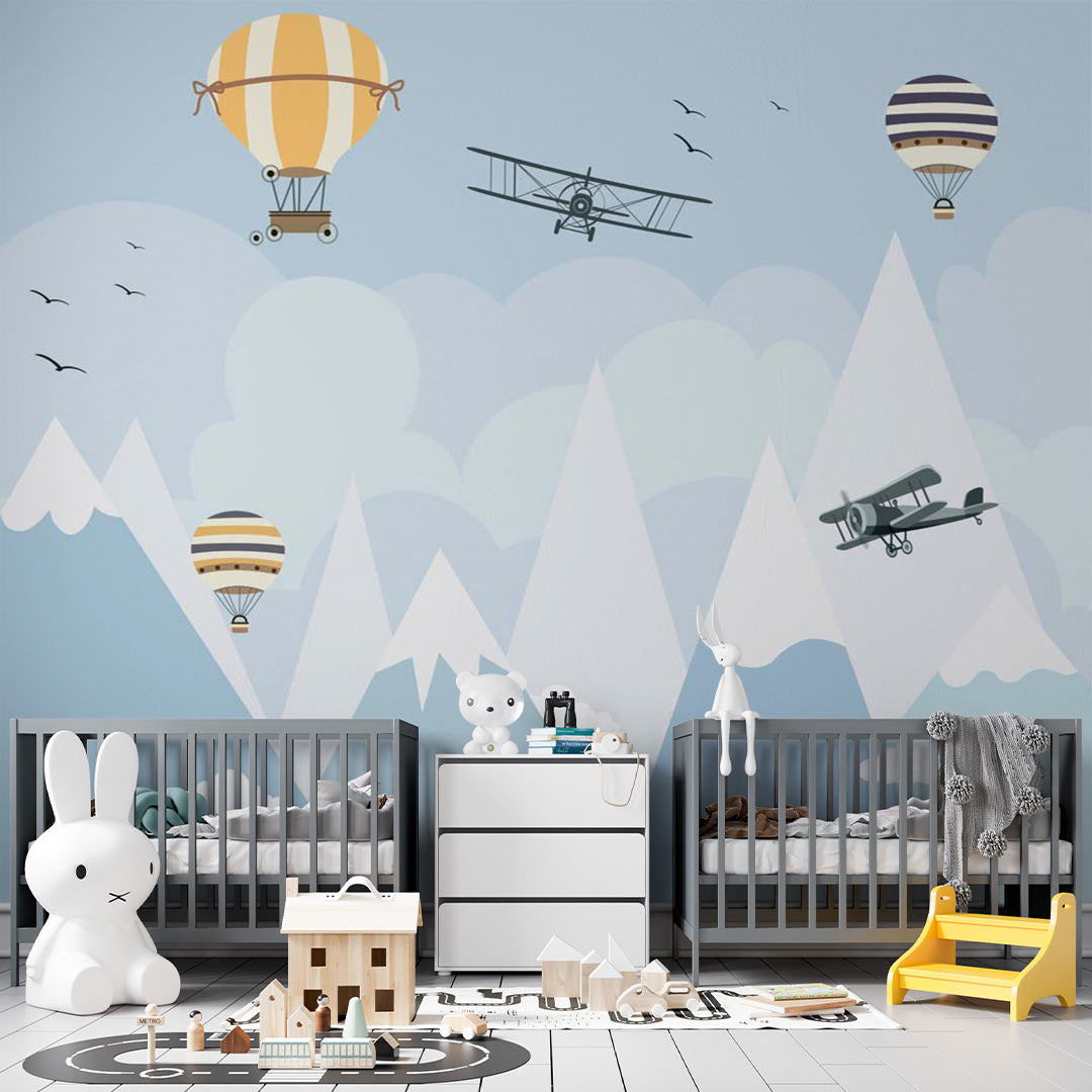 Blue nursery wallpaper with vintage airplanes and striped hot-air balloons flying above snowy mountains, clouds, and birds.