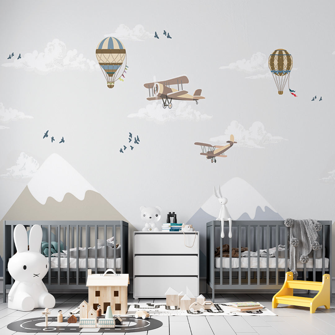 Pale blue nursery wallpaper with vintage biplanes and ornate hot-air balloons flying above snow-capped mountains, clouds, and birds.