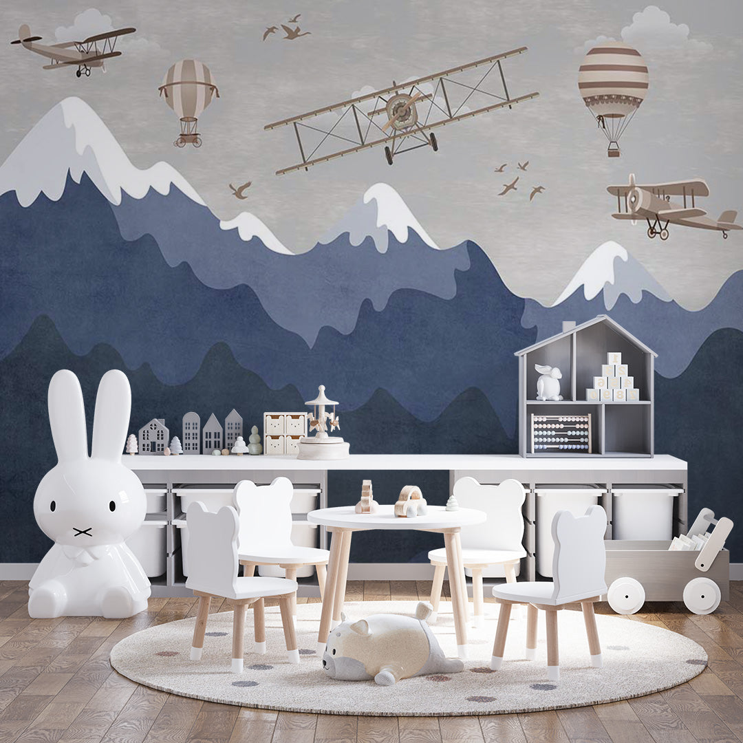 Kids room wallpaper with vintage biplanes and striped hot-air balloons flying above layered navy mountains, snowy peaks, and birds.