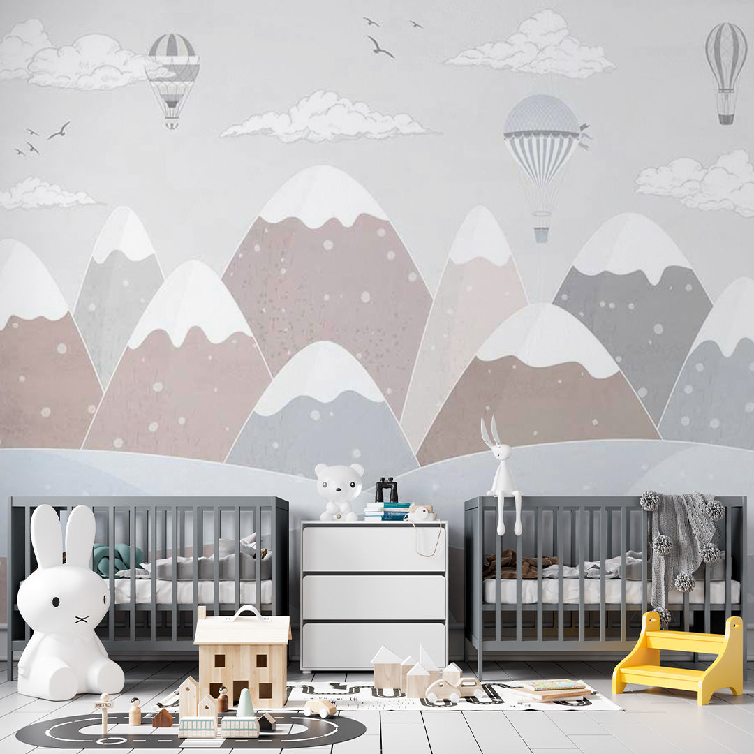 Pastel nursery wallpaper with hot-air balloons, clouds, and birds floating above softly textured snow-capped mountains.