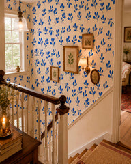 Cobalt blue leaf pattern wallpaper in a vintage-inspired stairway with sage green wall paneling and wood floor.