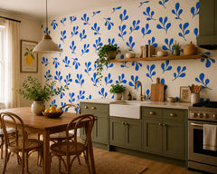 Blue botanical wallpaper in a cozy kitchen with olive green cabinets, farmhouse sink and natural wood dining table.