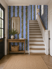 Blue stripe botanical wallpaper in an entryway with staircase and jute rug.