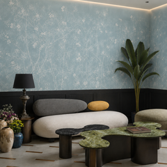 Dusty blue chinoiserie blossom wallpaper in a living room with black wainscoting and organic sofa.