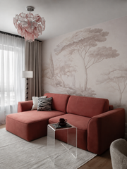 Blush pine landscape wallpaper behind a red sofa in a living room with pink chandelier.