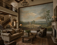Classic pastoral landscape wall mural in a grand living room with staircase and fireplace.