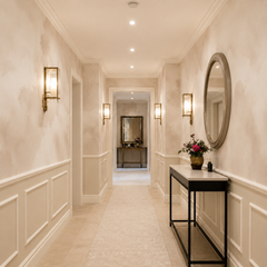 Soft beige watercolor wallpaper shown in an elegant hallway with wall molding, mirror and warm brass lighting.