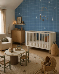 Blue grid wallpaper with tiny white figures in a nursery with a white crib and a play table.