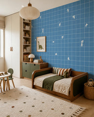 Blue grid wallpaper with tiny white figures in a boy’s bedroom with a wooden daybed and a dinosaur print.