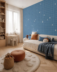 Blue grid wallpaper with tiny white figures in a kids’ bedroom with a low bed and a round rug.