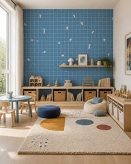 Blue grid wallpaper with tiny white figures in a playroom with low shelves and a round table.