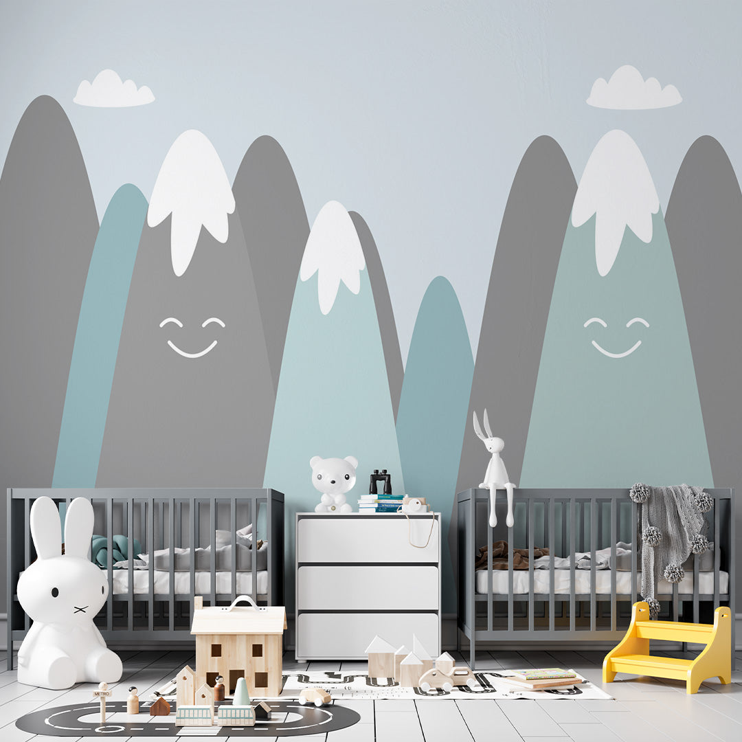 Minimalist kids room wallpaper with smiling blue and gray mountains, white snowcaps, and fluffy clouds on a pale blue background.