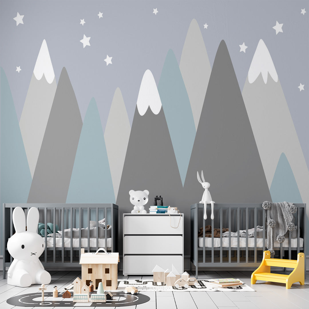 Blue nursery wallpaper with layered geometric mountains in dusty blue, gray, charcoal, and cream, with white snowcaps and stars.