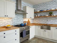 Fish pattern wallpaper in a white coastal kitchen with wood countertops and navy blue accessories.